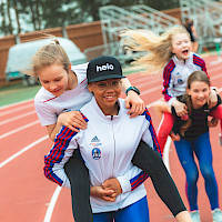 Hymyileviä lapsia kantamassa toisiaan reppuselässä urheilukentällä