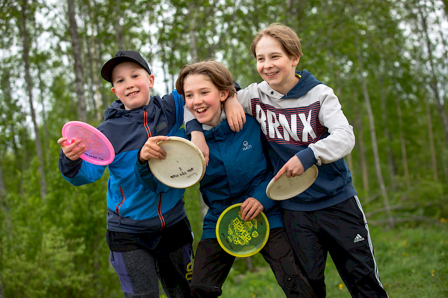 Kolme hymyilevää nuorta frisbeet käsissä