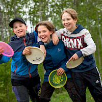 Kolme hymyilevää nuorta frisbeet käsissä